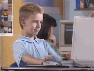 A boy sitting in front of a computer giving thumbs up